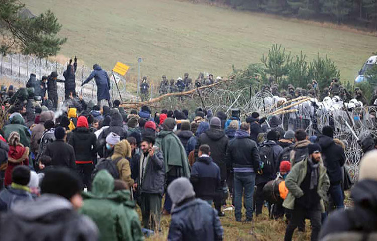 Migrantes param na cerca de arame farpado. Foto Leonid Scheglov